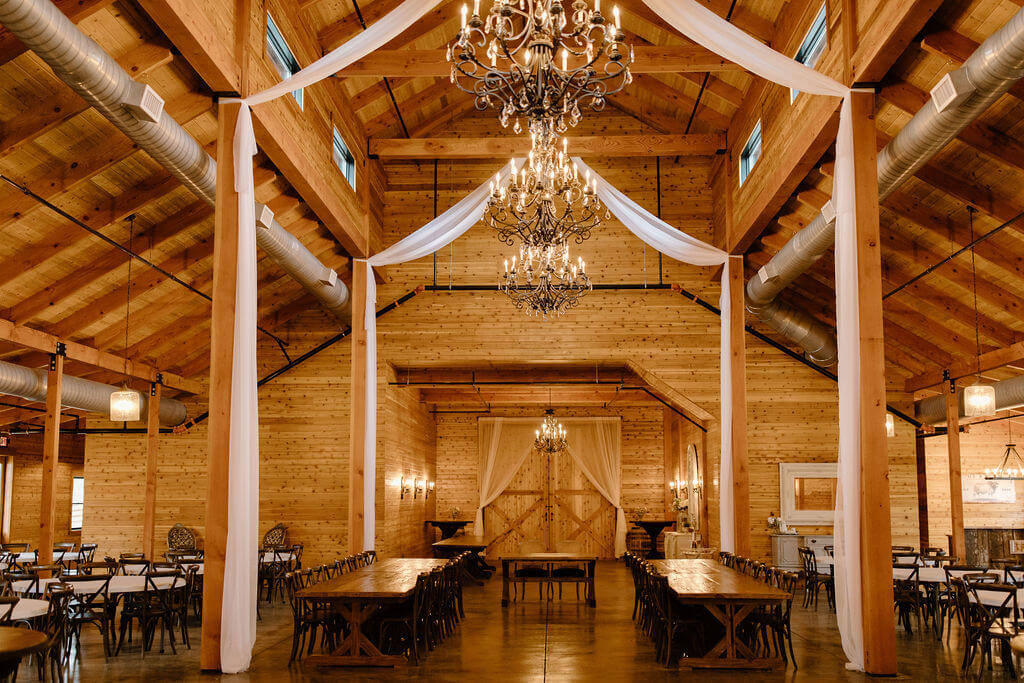 Inside of The Dogwood Barn with tables and chairs below and chandeliers above